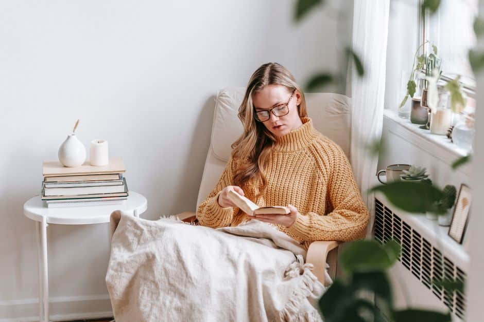 Lectrice plongée dans un roman dans un fauteuil, livres et bougie posés à côté d'elle