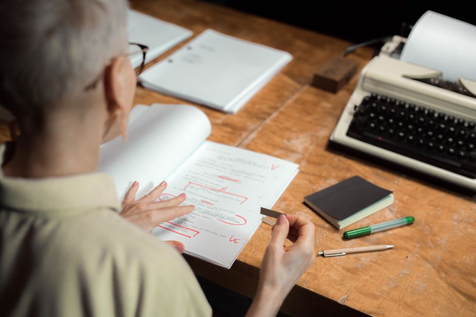 Autrice relisant un manuscrit imprimé couvert d'annotations au stylo rouge, près d'une machine à écrire